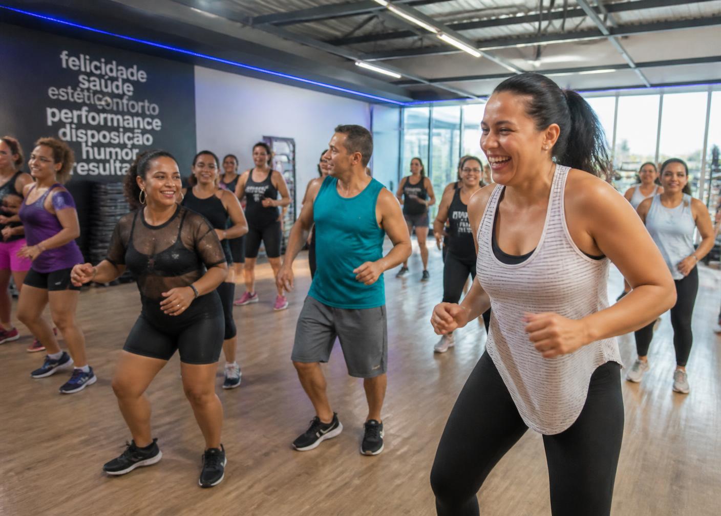 Aula coletiva de dança na Conexão Fit com alunos sorrindo